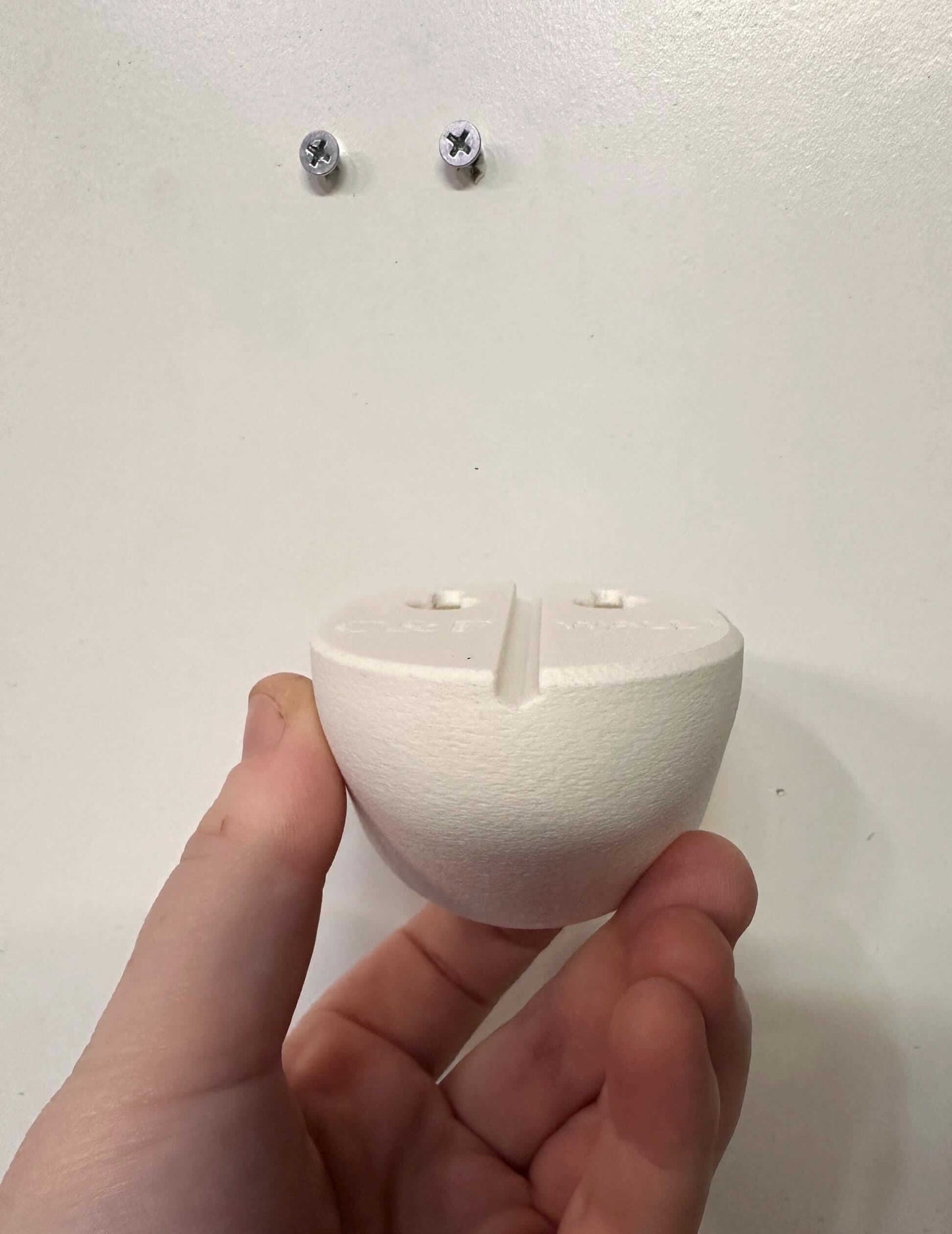 Owlet Baby Monitor Wall Mount | Angled | Cam 2 hand-held view showing back of mount for easy installation and no drill system.
