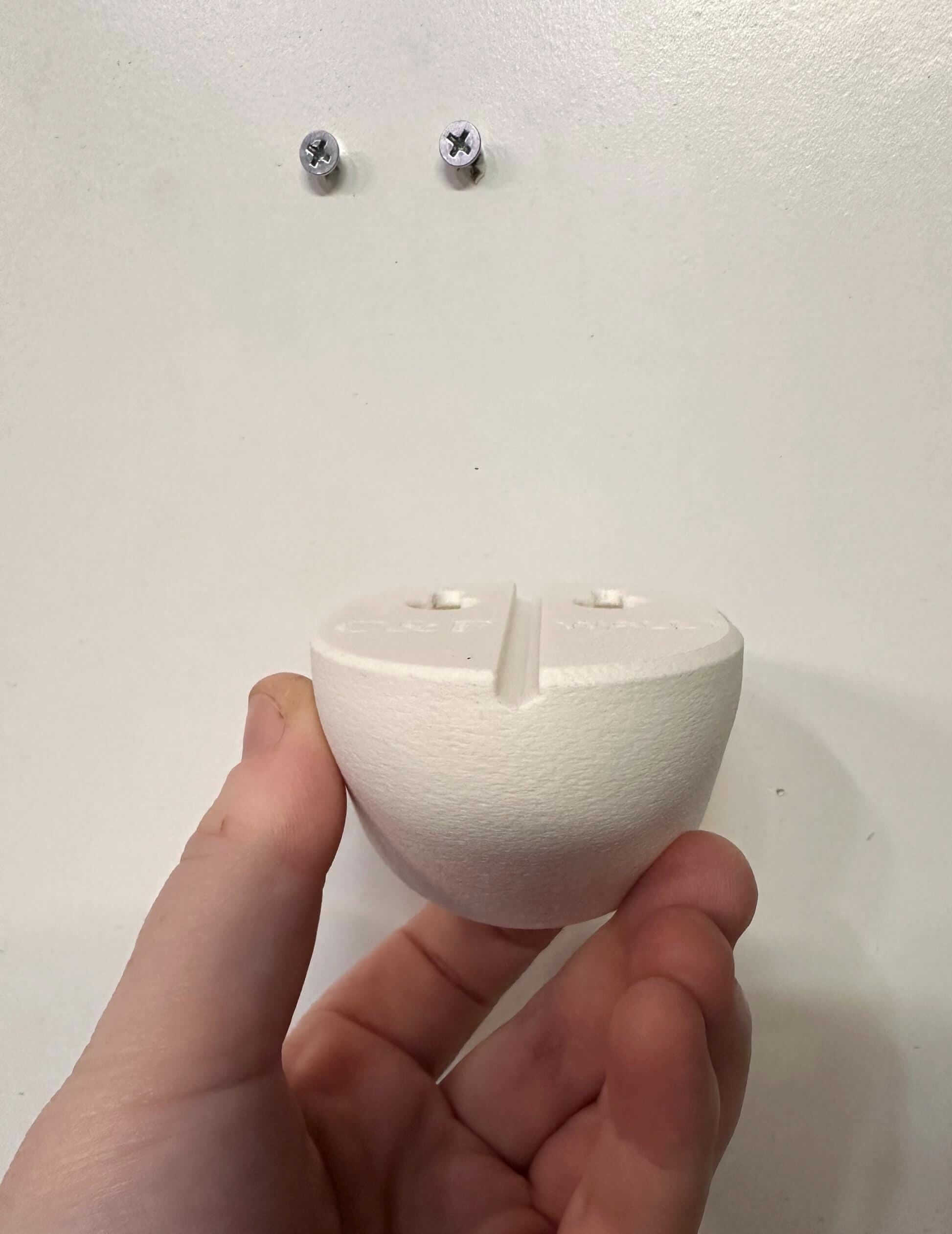 Owlet Baby Monitor Wall Mount | Angled | Cam 2 hand-held view showing back of mount for easy installation and no drill system.